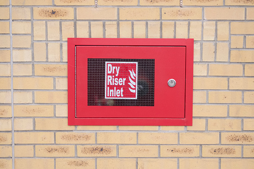 Dry riser inlet box red on brick wall for emergency fire services water connection for hose brigade engine at shopping mall retail park uk